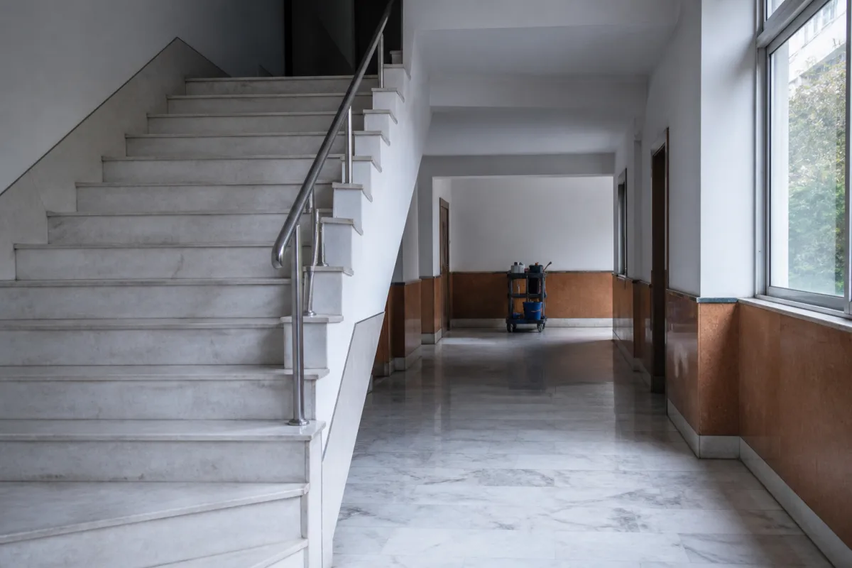 Καθαρή είσοδος και κλιμακοστάσιο πολυκατοικίας με καρότσι καθαρισμού στο βάθος